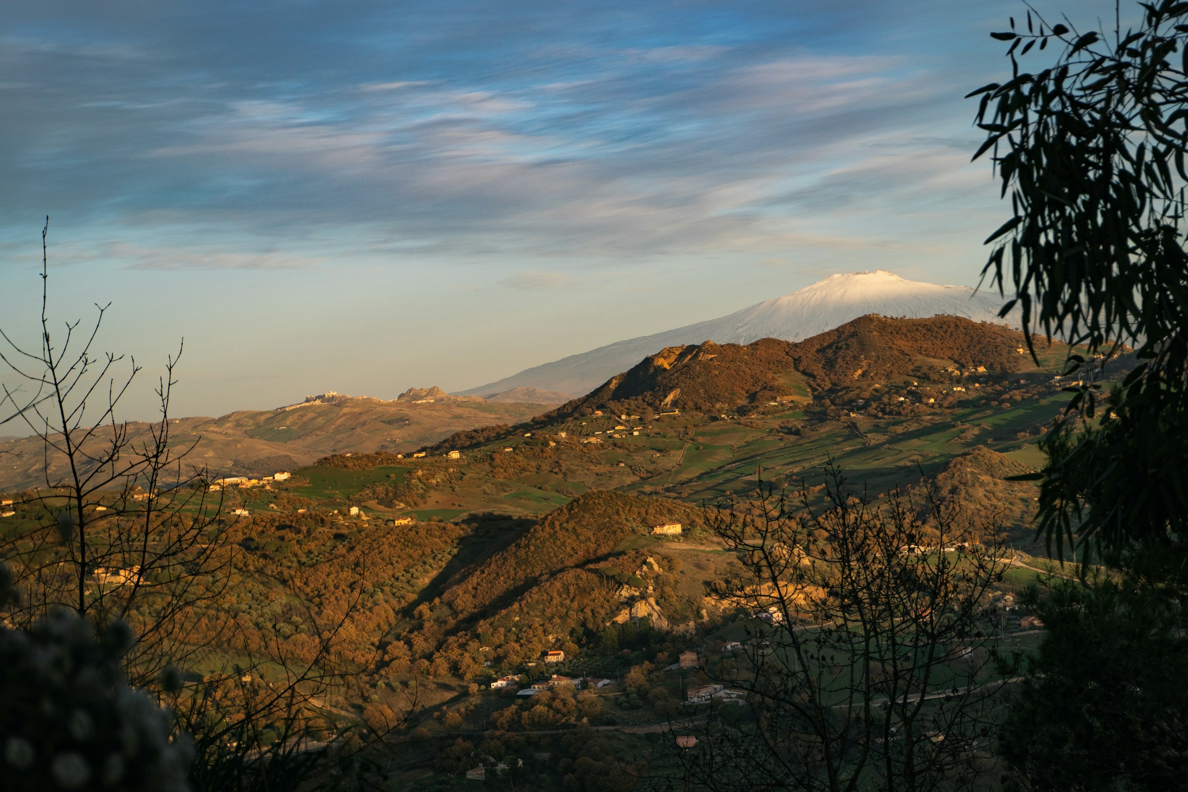 Mt Etna rising beyond sun-baked golden Sicilian hills and terraced rural countryside.