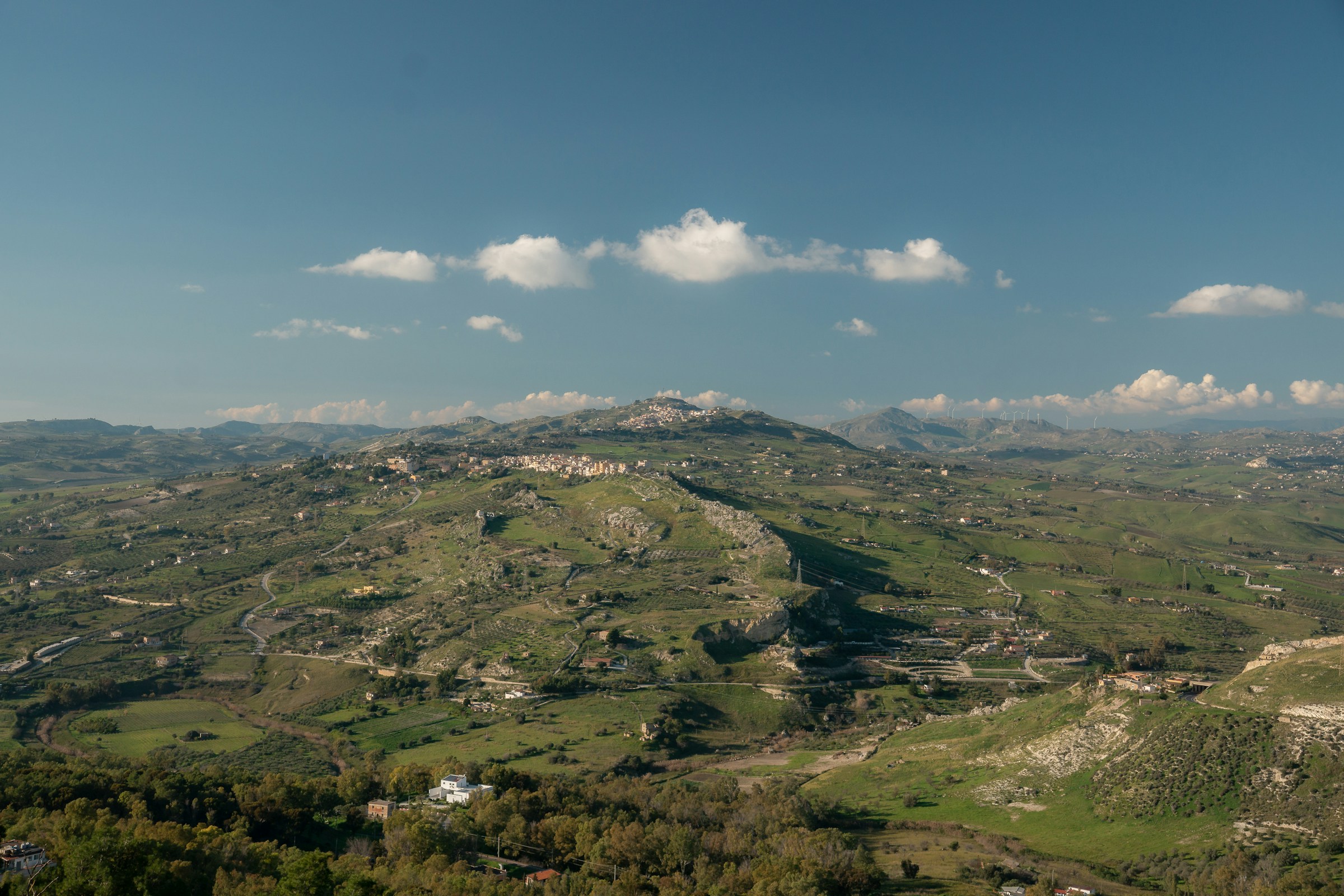 Rolling cultivated hills and hilltop town in southern Sicily under blue sky.
