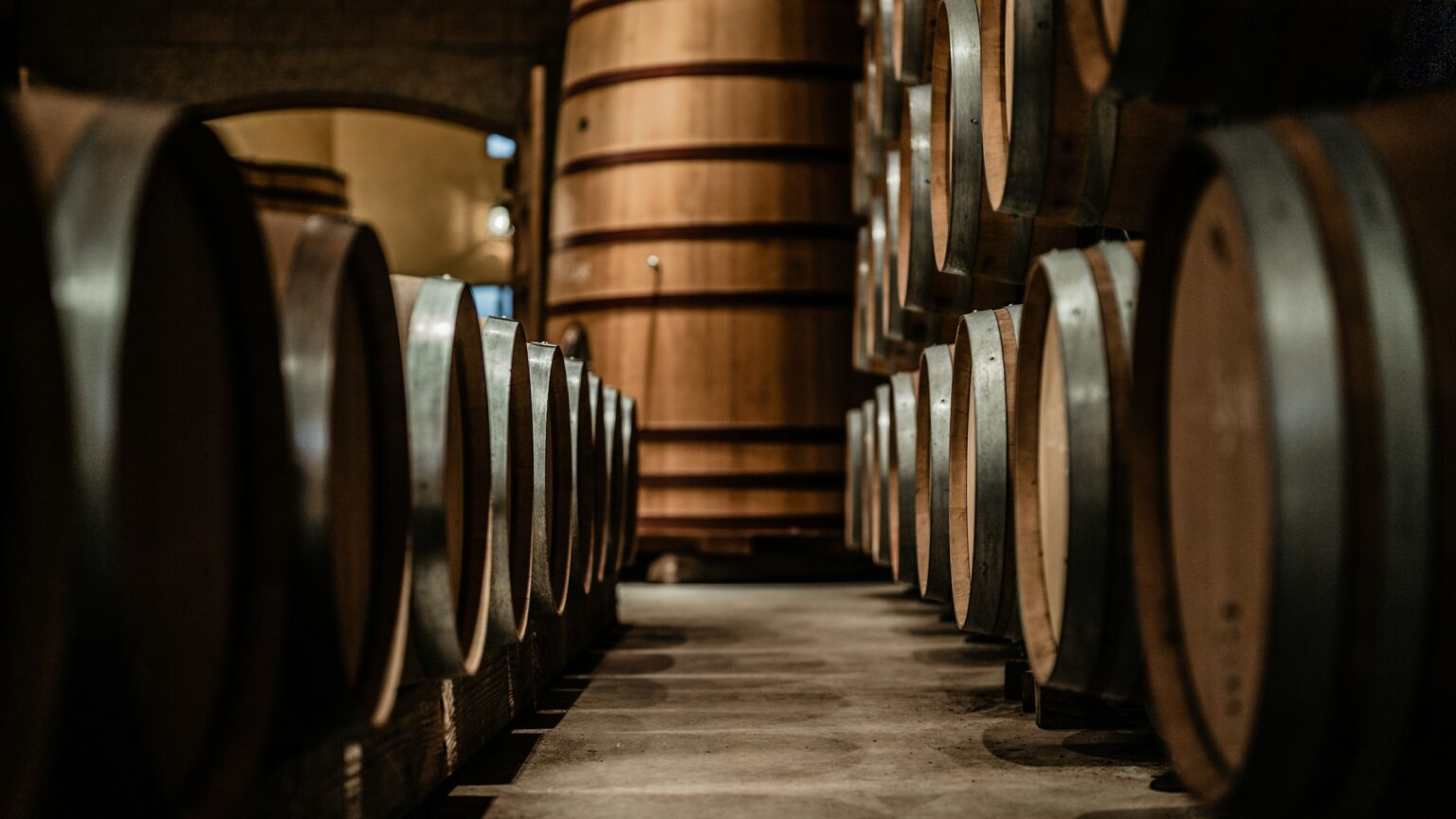Sherry’s Indie Comeback: Why Jerez’s Young Producers Are Unfortifying The Future Wine-barrel cellar corridor with central foudre and side barrels in a classic chai-register space, evoking the aging halls where Jerez's indie producers are reframing the sherry category around terroir.