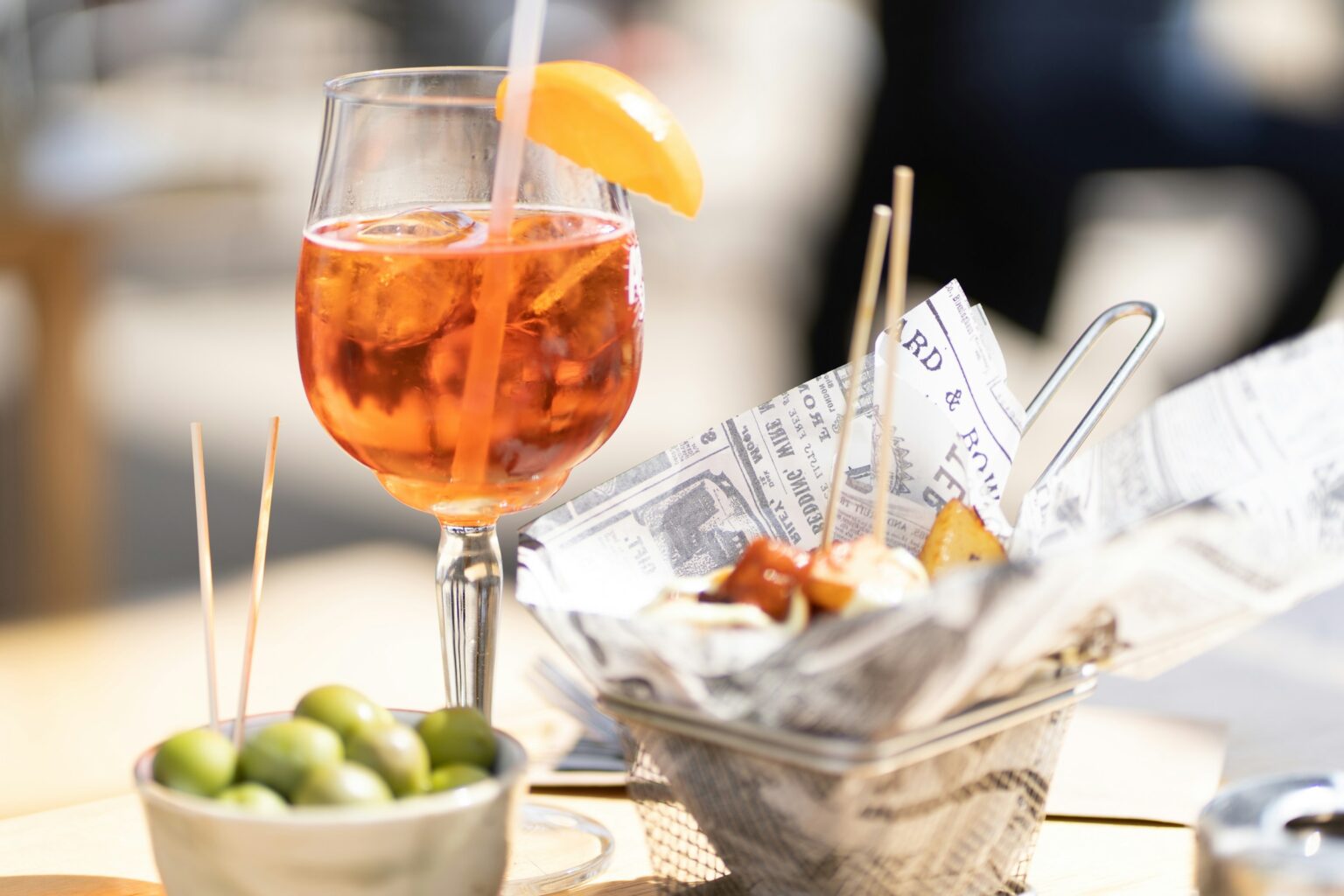The Aperitivo Question: Why The Pre-Dinner Pour Is Suddenly Everywhere An Italian aperitivo laid out at golden hour before dinner: a bittersweet spritz, olives, and small bites on a café table.