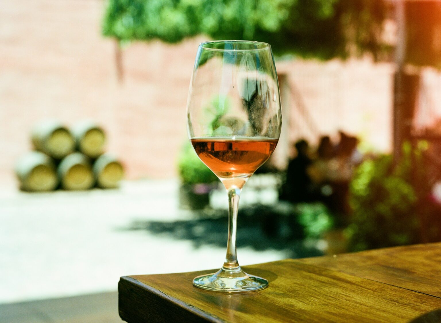 Saignée or Direct Press: Why Rosé’s Color Is a Record, Not a Verdict A glass of pale salmon rosé on a wooden table before a stack of barrels, the color recording a pressing decision rather than a quality grade.