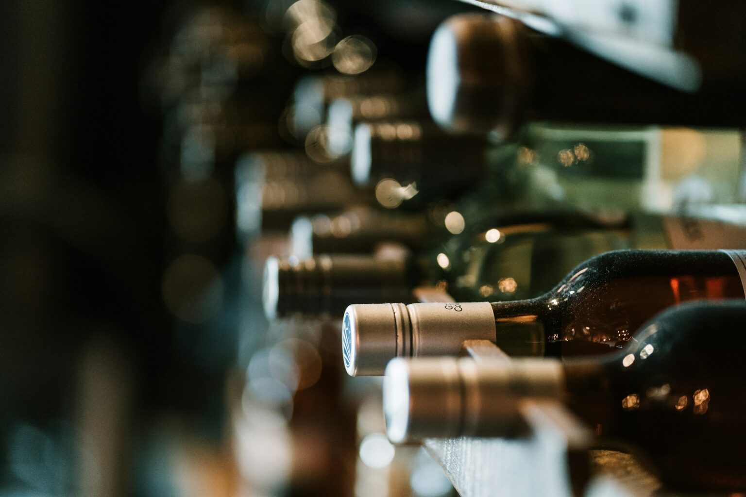Rows of fine wine bottles resting on their sides in a dim cellar rack, capsules catching the light